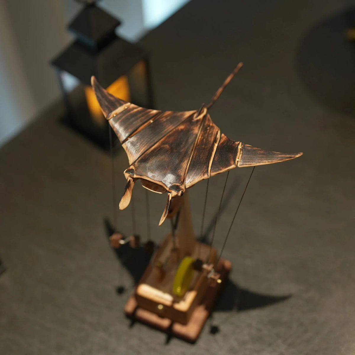 Close up of the copper-toned ribbed wings of the manta ray automaton, lantern glow behind.