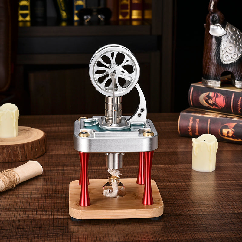 Metal Stirling engine on red legs and a bamboo base, with a flywheel and a small lamp underneath, beside books and candles