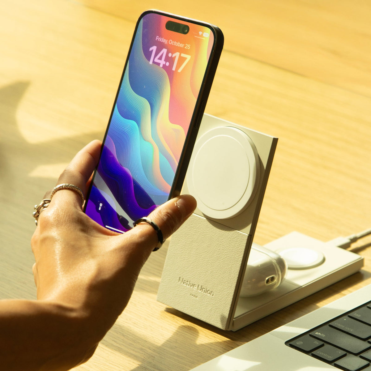 Hand holding a phone on the sandstone charger stand on a wooden desk