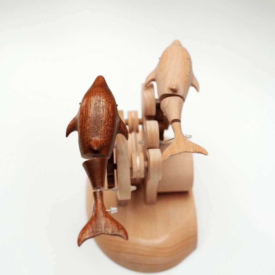 The pair seen from behind: the dark dolphin and a pale one above the carved base.