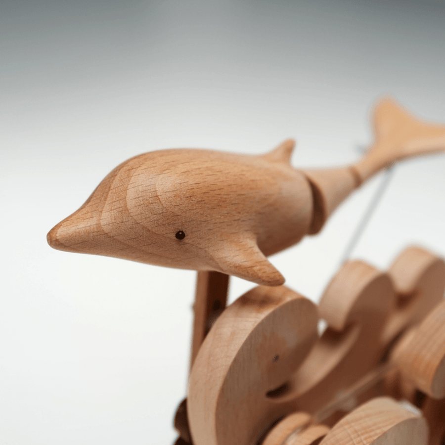 The pale dolphin head and body, close up, above the carved waves.