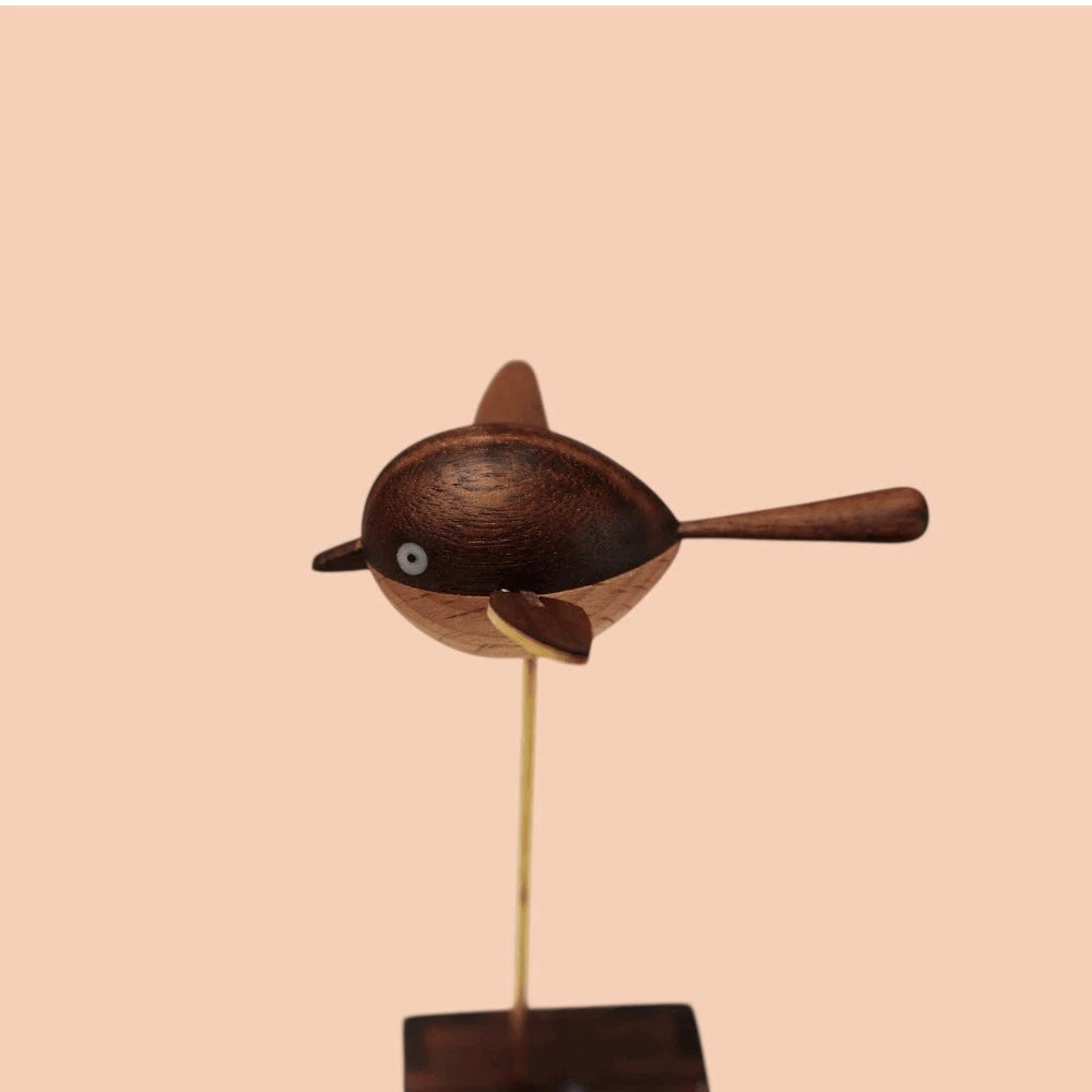 Side view of the round wooden bird with its wings out, short beak and a small white eye, on the brass rod.