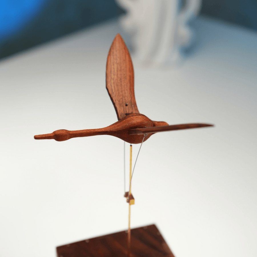 Walnut swan from the side with its wings up above the box, a plain wall behind.