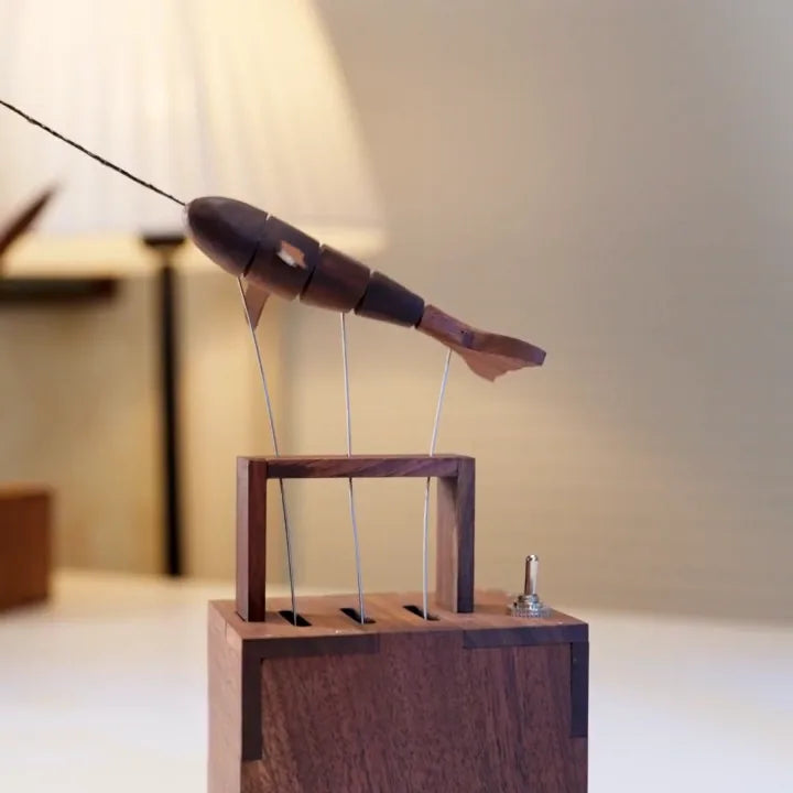 dark wood whale with a white fin above its dark wood frame, pleated lamp glowing behind on a white shelf.