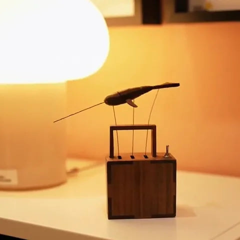 Dark whale shape on wires above the dark wood box in front of a glowing orange lamp.