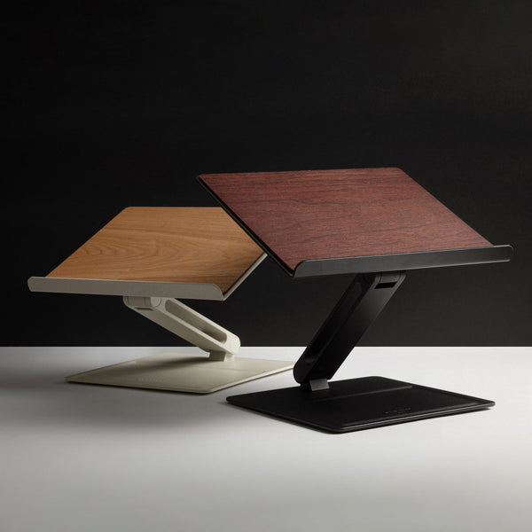 Two desk laptop stands, one with a light wood top and cream base and one with a dark wood top and black base, on a dark backdrop