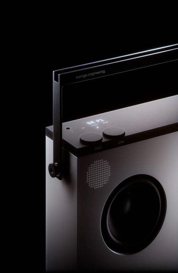 Close-up of the OB-4 top handle, two knobs and one round woofer on a dark backdrop