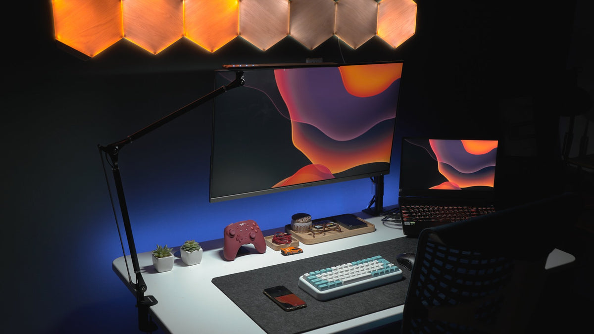 Dark desk with a monitor arm, light bar and warm wood hexagon wall lights