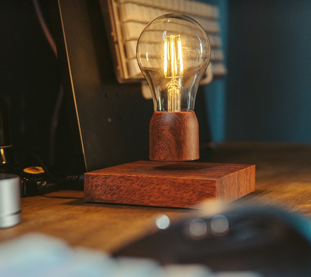 Levitating bulb lamp on a walnut base on a wood desk