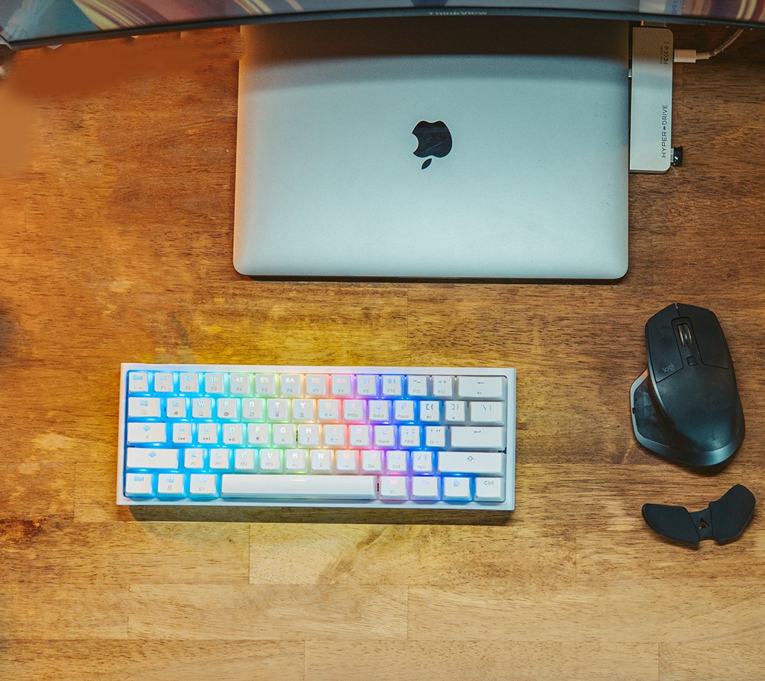 Top-down view of a closed laptop, RGB mechanical keyboard and ergonomic mouse on a wood desk
