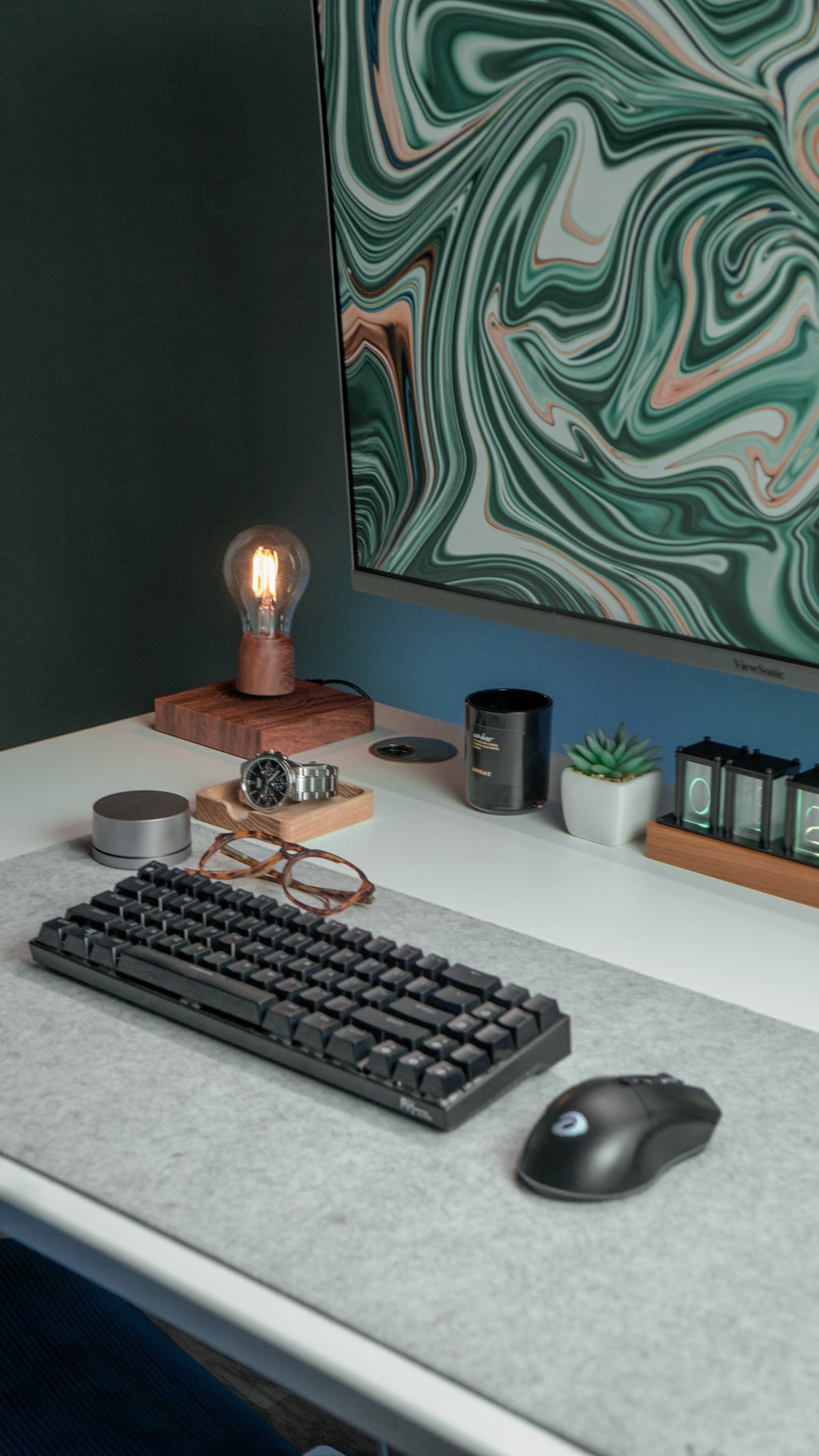 Black keyboard, mouse and Edison lamp on a white desk under a green marble screen