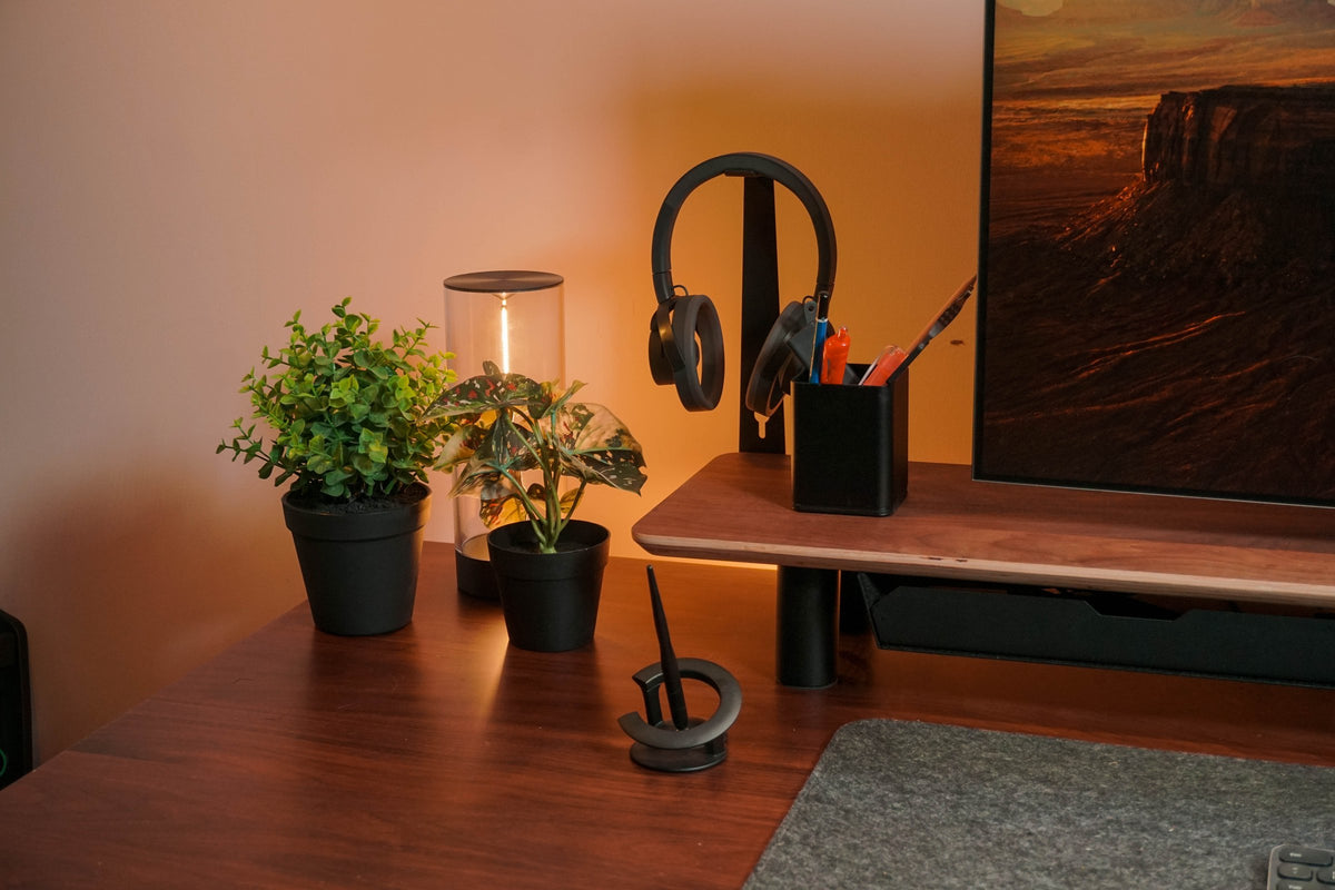 Headphone stand, pen cup and plants on a walnut desk beside the monitor