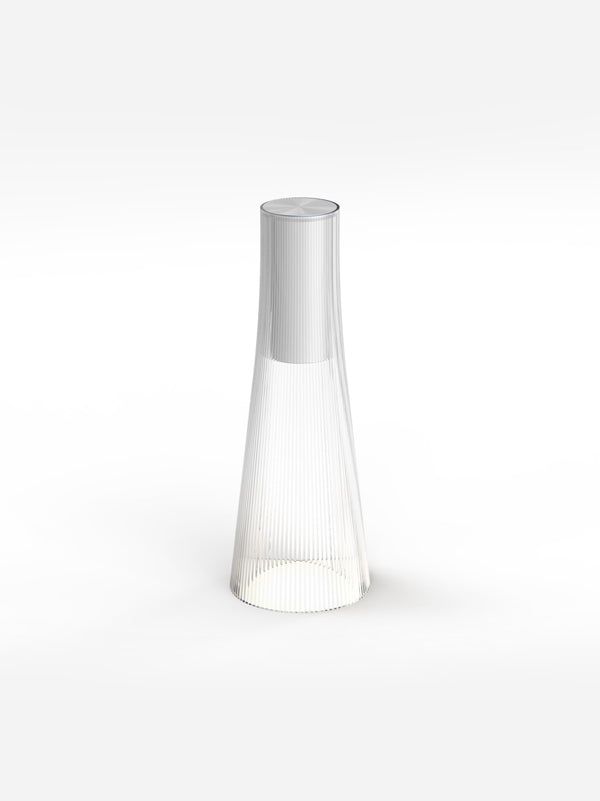 The clear Candel lamp, a tapered fluted cone with a silver cap, glowing at the base on a pale background