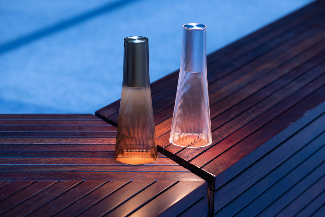 Two Candel lamps, one smoke and one clear, lit on a dark wooden deck at dusk