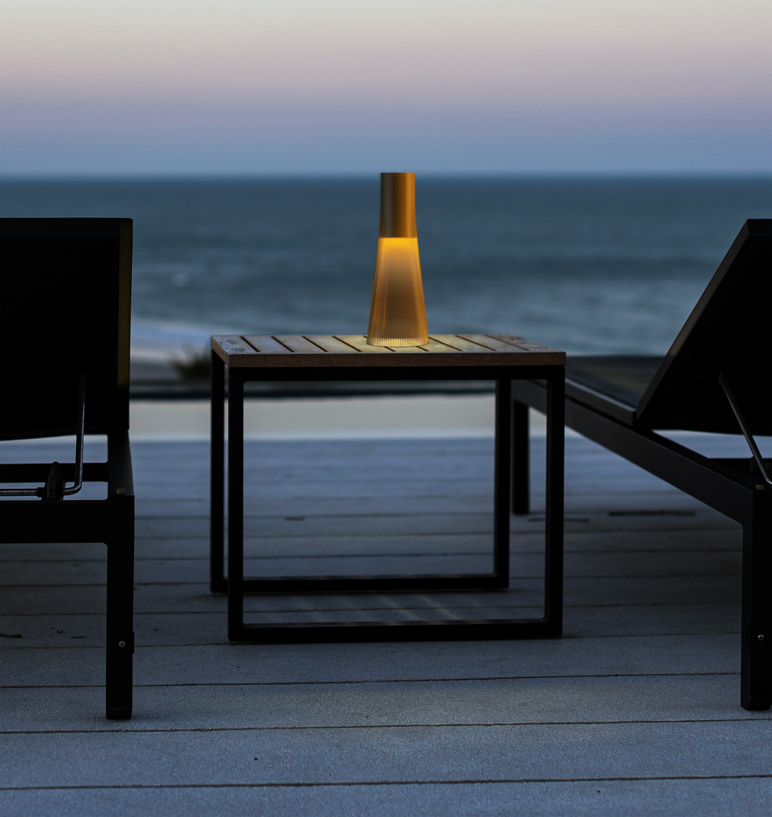 An amber Candel lamp glowing on a small table with the sea behind at dusk