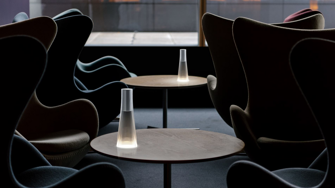 Two Candel lamps lit on small round tables between dark armchairs