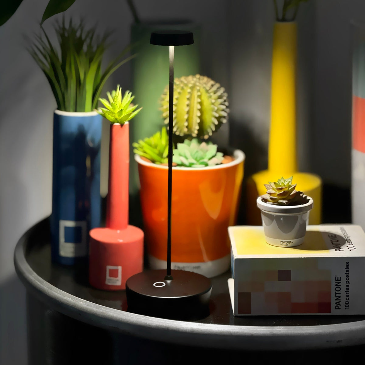 A black Swap Pro lamp lit on a round tray among colorful pots and a small cactus