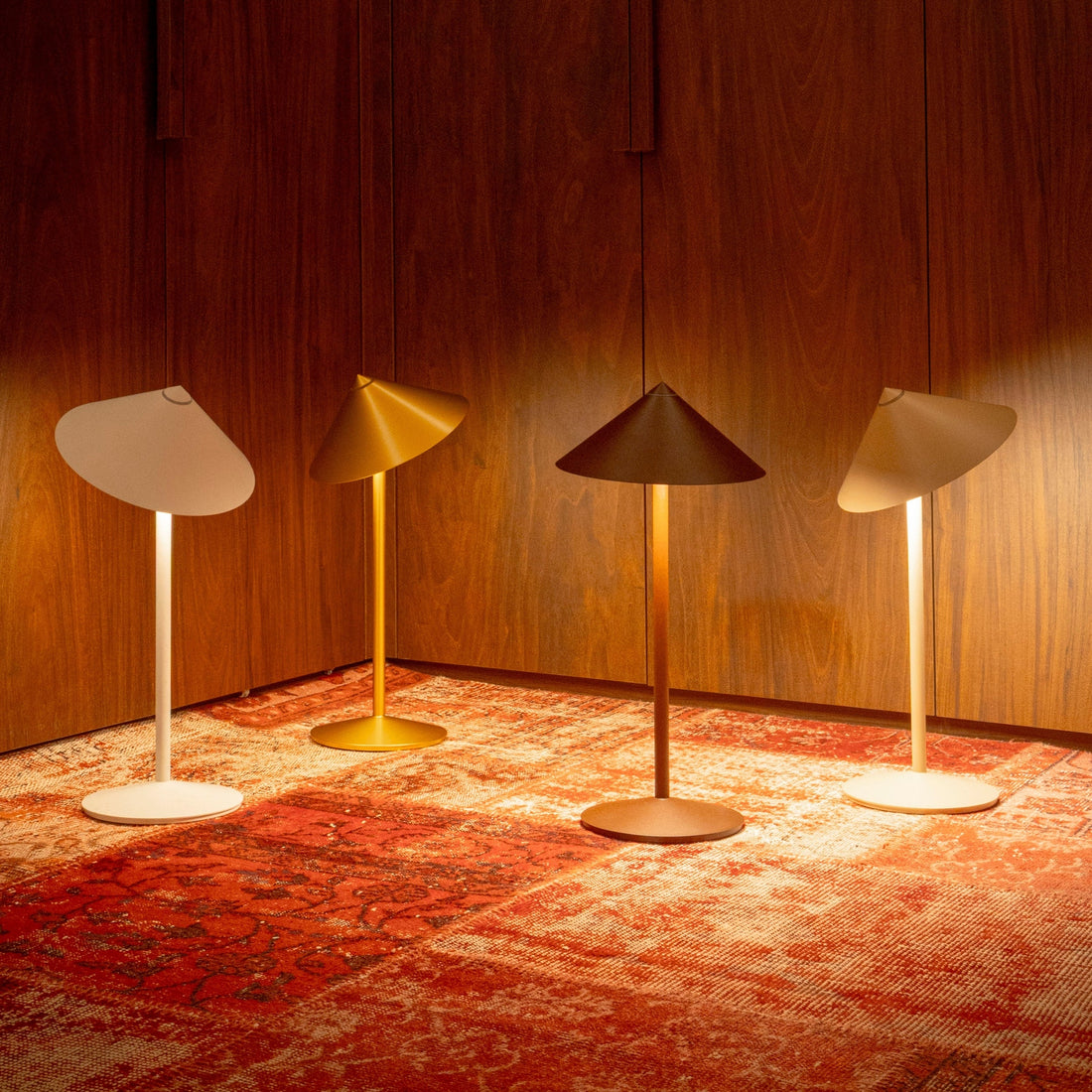 Four Pina lamps in white, gold, bronze and cream finishes glowing on a patterned rug