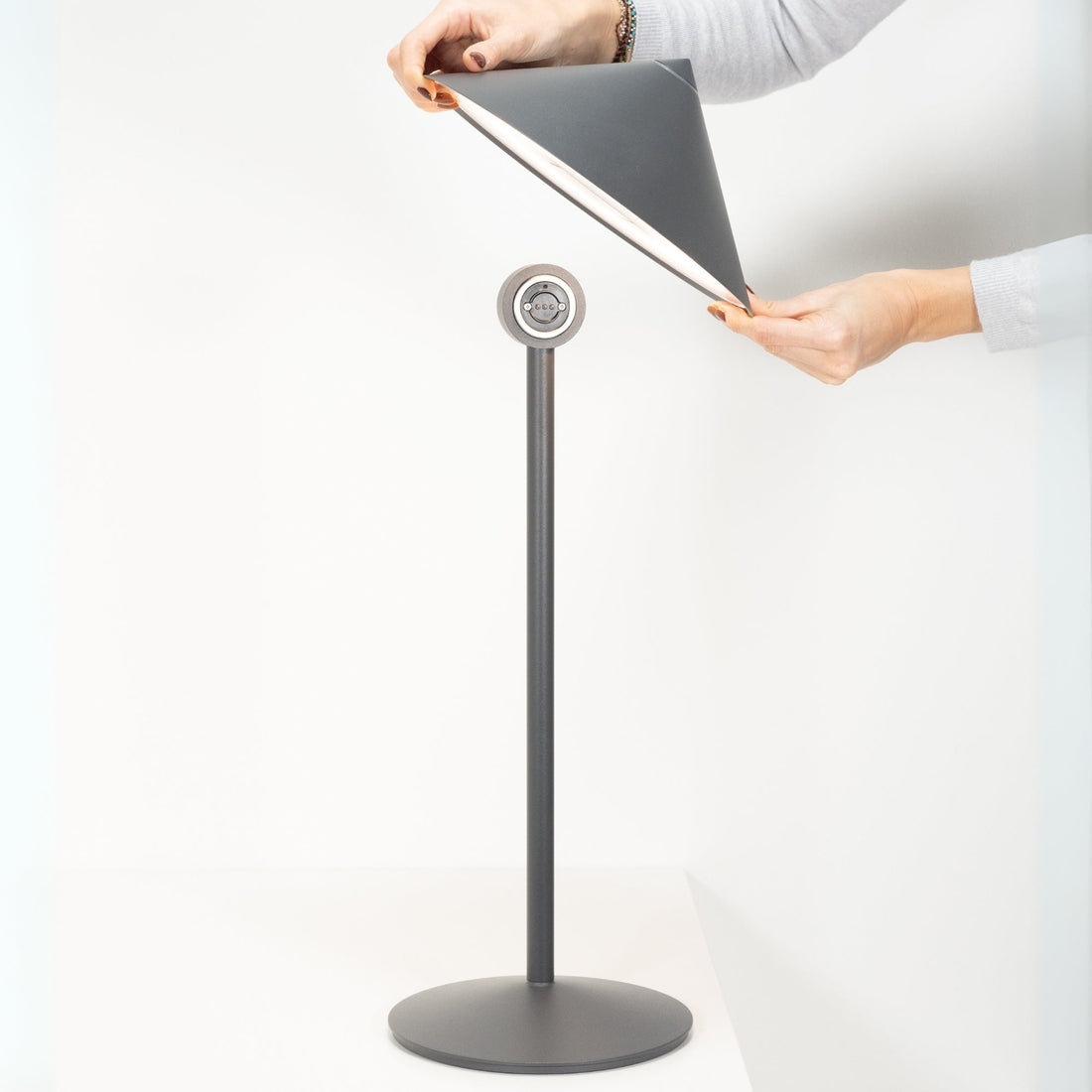 Two hands tilting the grey cone head of the lamp on its magnetic joint