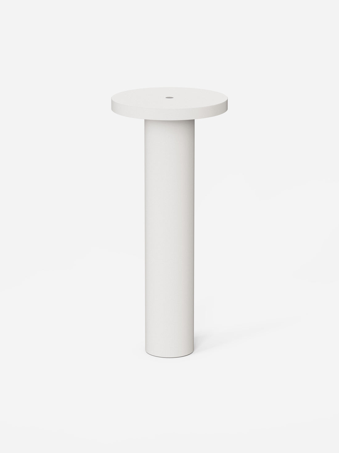 The white Luci table lamp, a slim machined cylinder with a flat round top, on a pale background