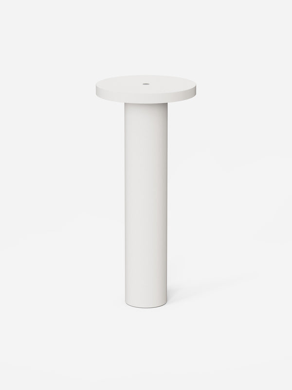 The white Luci table lamp, a slim machined cylinder with a flat round top, on a pale background