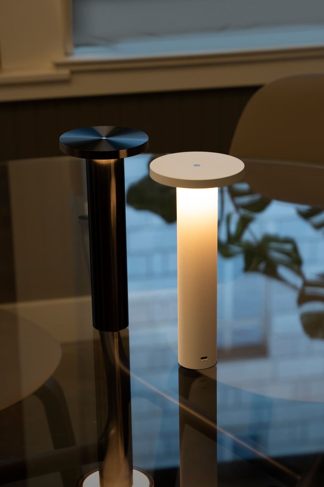 A black Luci and a white Luci glowing side by side on a glass table