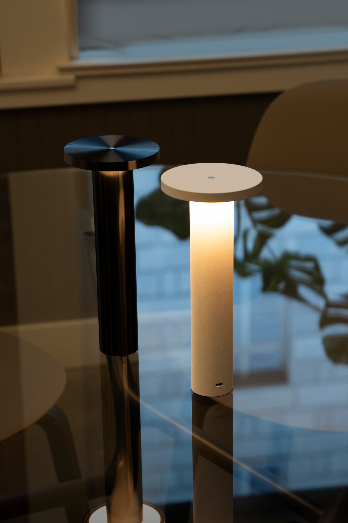 A black Luci and a white Luci glowing side by side on a glass table