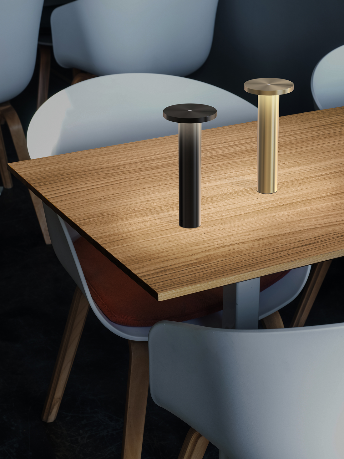 A black and a brass Luci lamp on a wood-top table among chairs