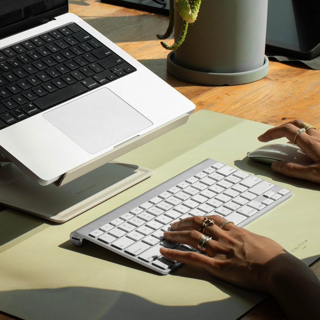 Laptop on the sandstone stand above a green desk mat with a keyboard and mouse, hands typing