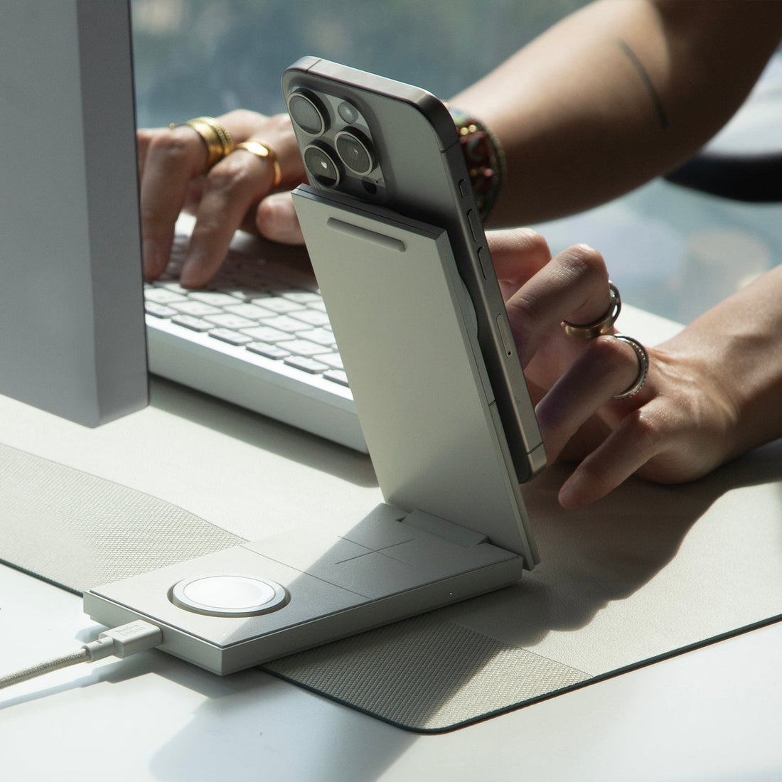 Phone attached to the charger on a desk beside a keyboard, hands typing