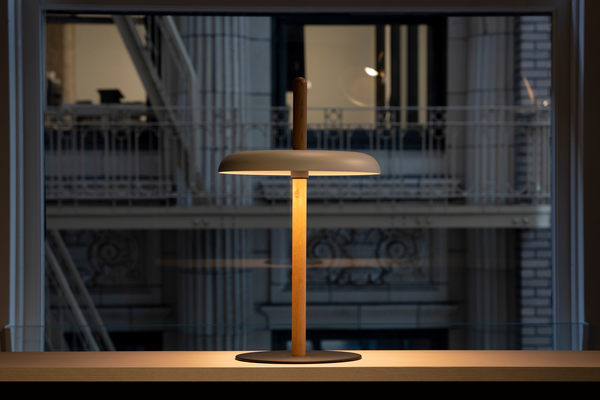 The Nivel lamp glowing warm on a ledge in front of a city window at night