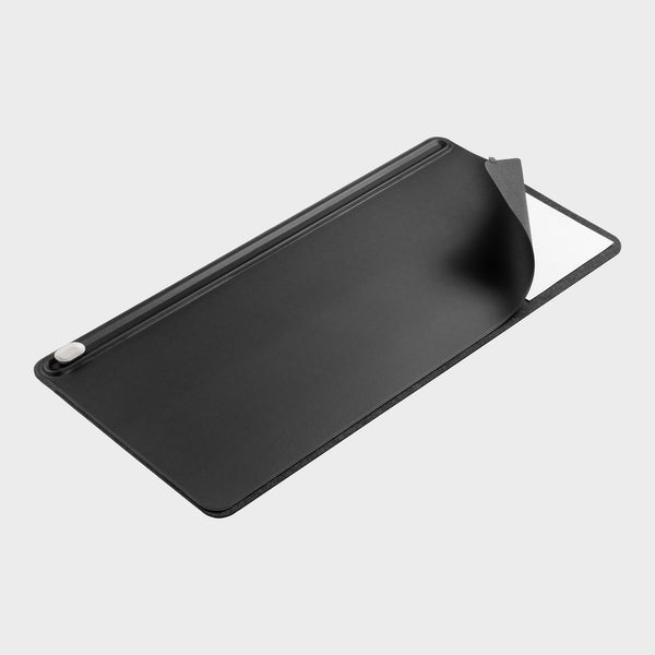 Black desk mat seen at an angle with one corner lifted to show a white sheet underneath, and a clip at the top edge