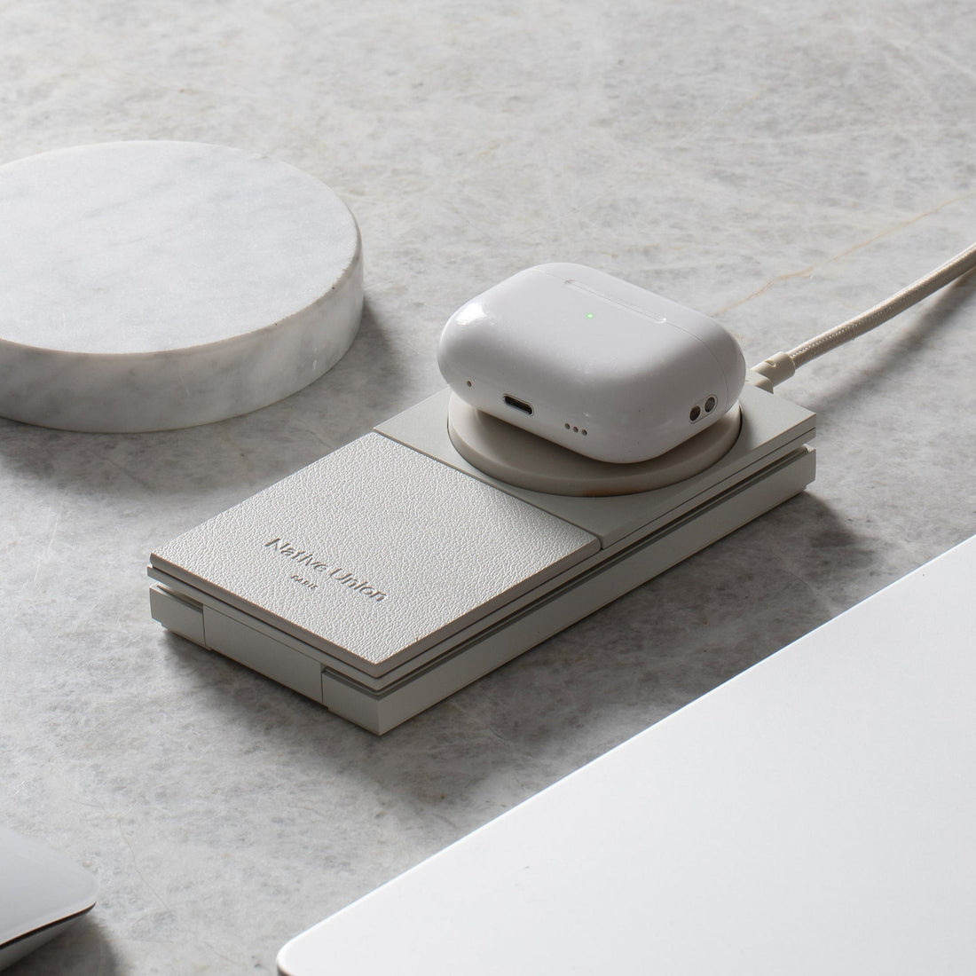 Earbuds case resting on the folded charger on a marble surface beside a round stone dish