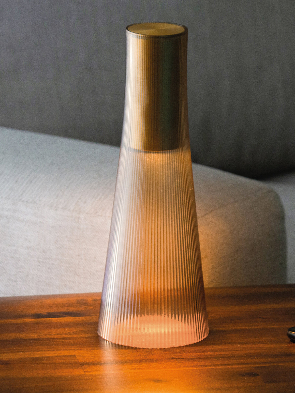 A bronze Candel lamp glowing warm on a wooden table in front of a sofa