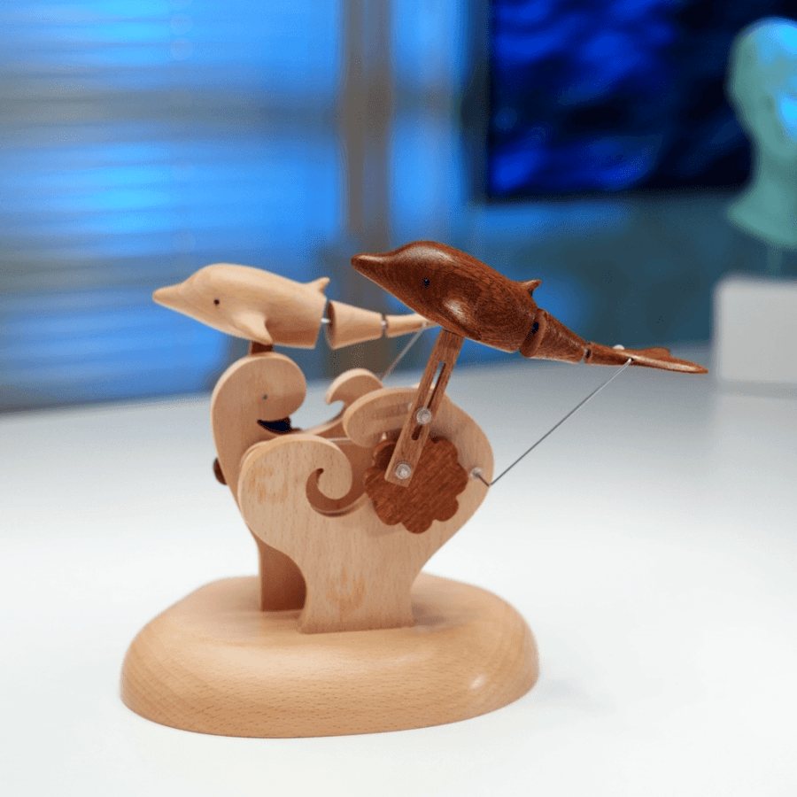 Both dolphins mid-leap over the carved waves on the pale wood base in a blue-lit room.