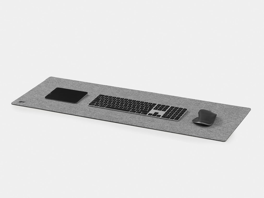 Grey felt desk mat at an angle with a keyboard, trackpad and mouse