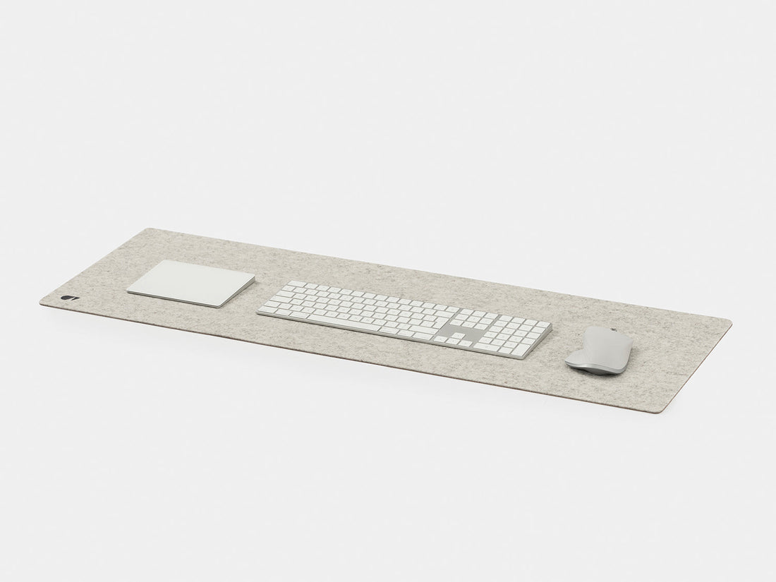 Stone grey felt desk mat at an angle with a white keyboard, trackpad and mouse