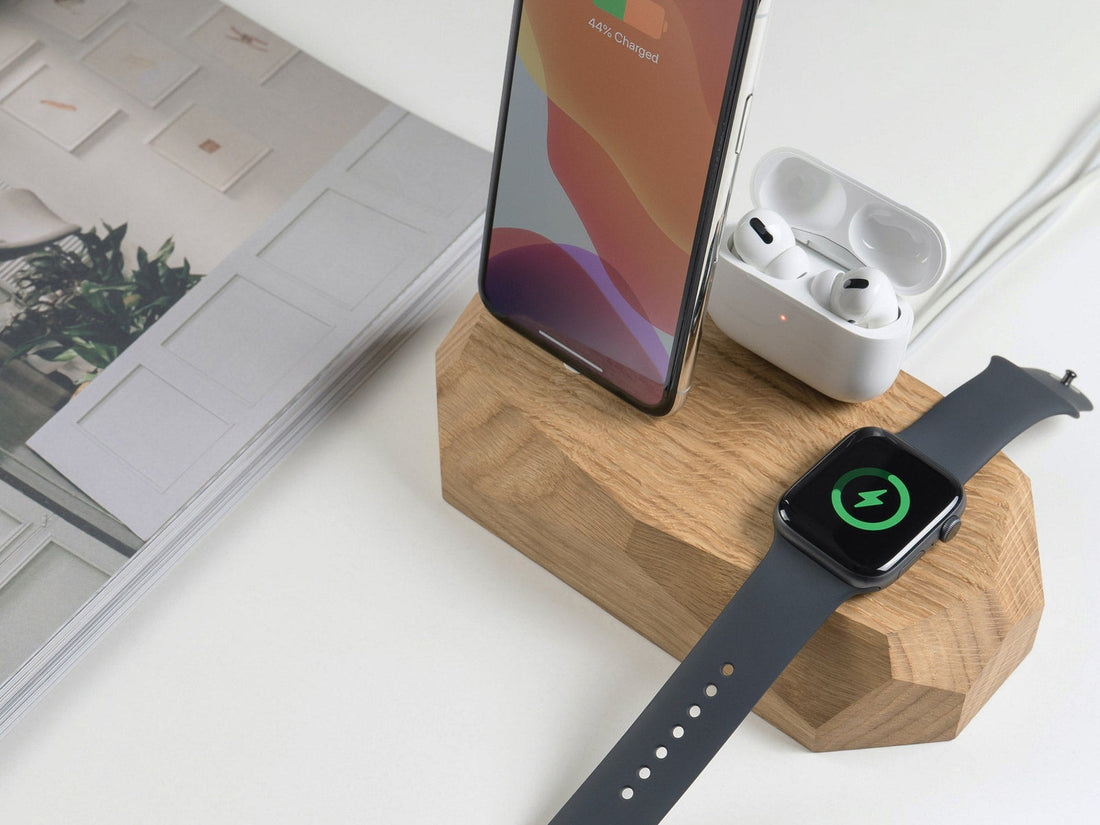 Phone, earbuds case and watch on an oak dock beside a magazine, the watch showing a charging symbol