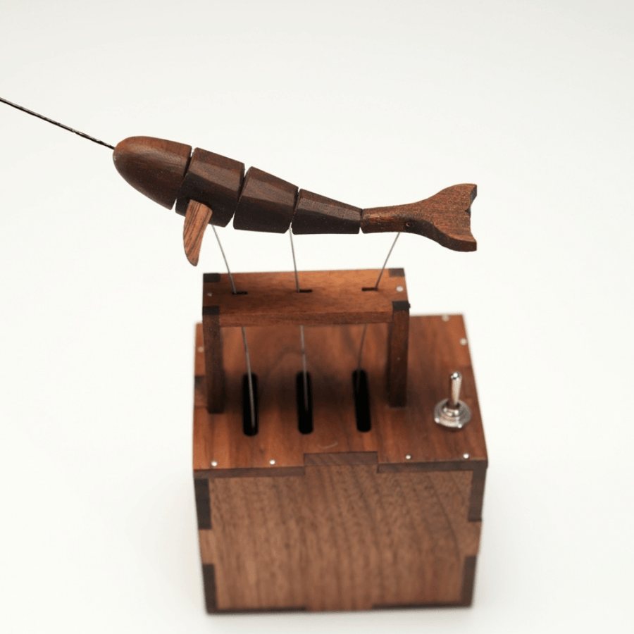 Narwhal from the front above its dark wood box, tusk reaching out, three wires and a small toggle switch.
