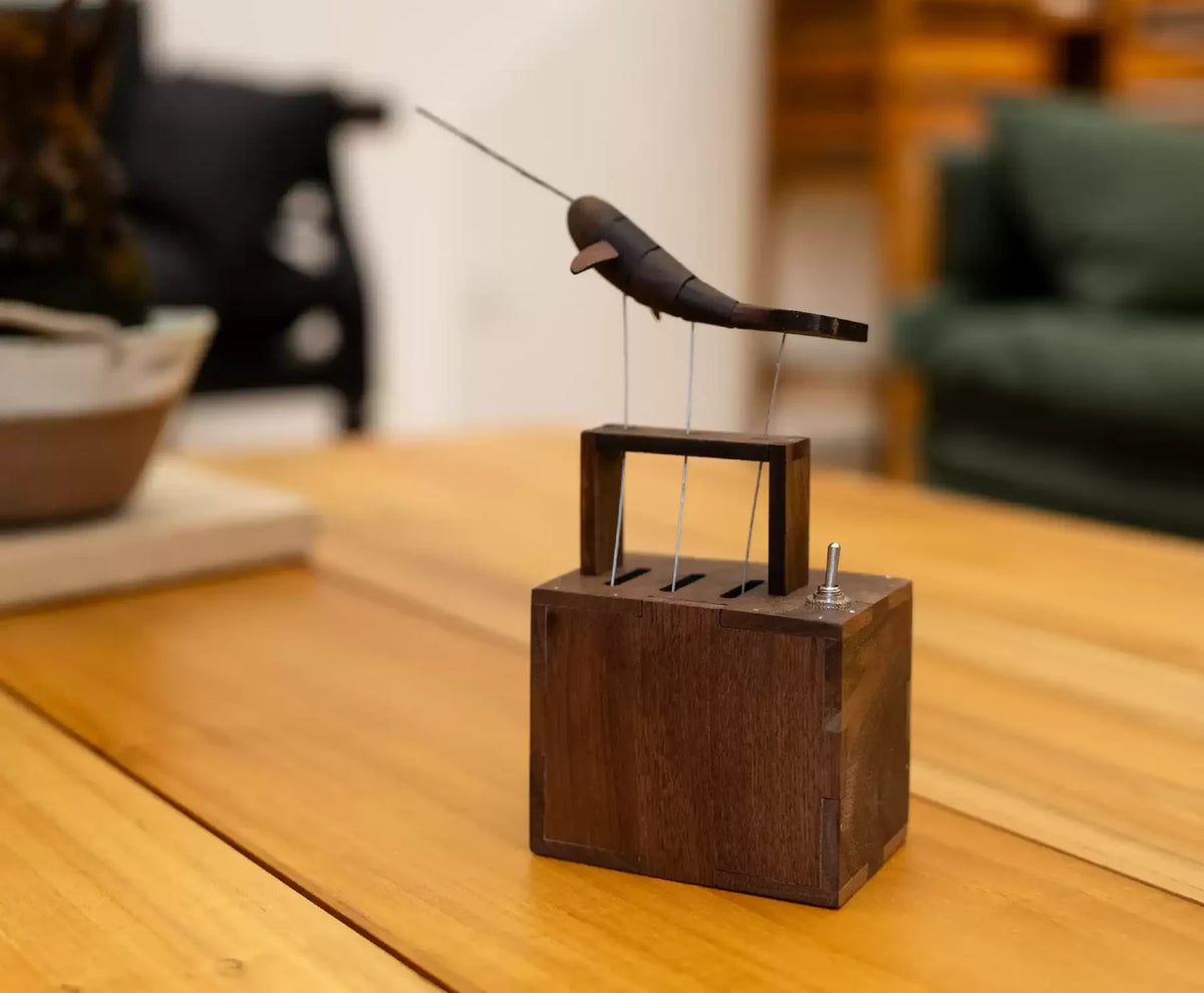 The narwhal automaton on a wooden table, a shelf and green chair blurred behind.