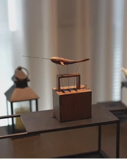 Narwhal automaton beside a lantern on a dark sideboard, window blinds behind.