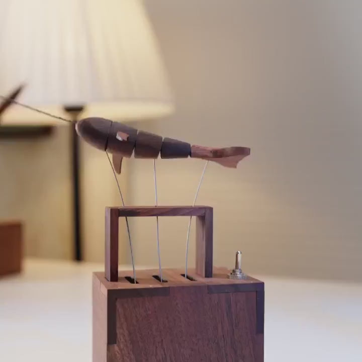 Narwhal automaton under a lamp, three wires rising from the dark wood box.