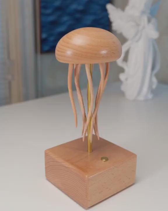 Light wood jellyfish automaton on a square wood base, tentacles swaying, a white statue and a blue picture blurred behind.