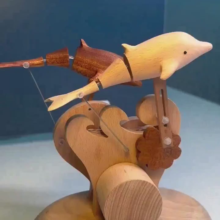 Two dolphins leaping together over carved wooden waves, seen from the side against a blue wall.