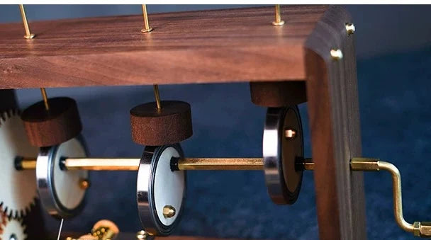 Close view inside the dark wood frame: the gear wheel, three cams on a brass shaft and the rods they lift.