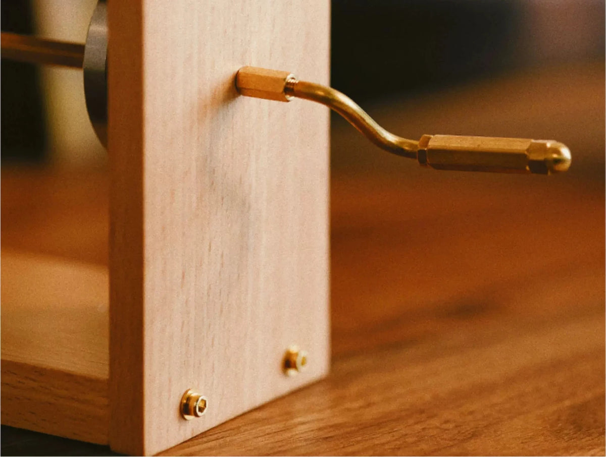 The brass crank on the side of the pale wood frame, close up, on a wooden table.