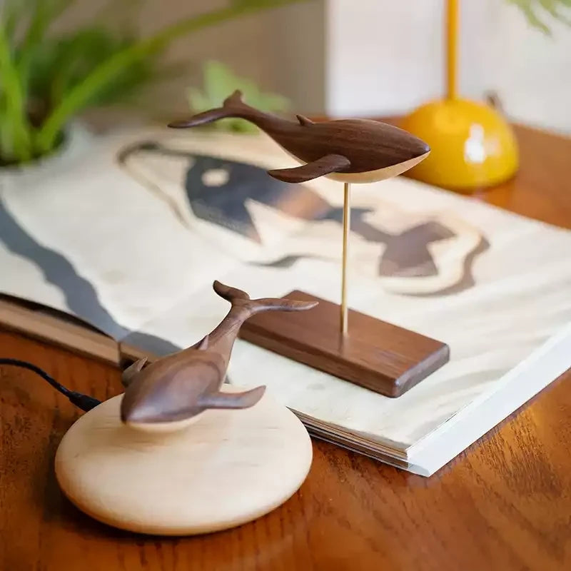 Both editions on a desk: the walnut whale floating above its maple base and a second whale on a brass rod above a walnut stand.